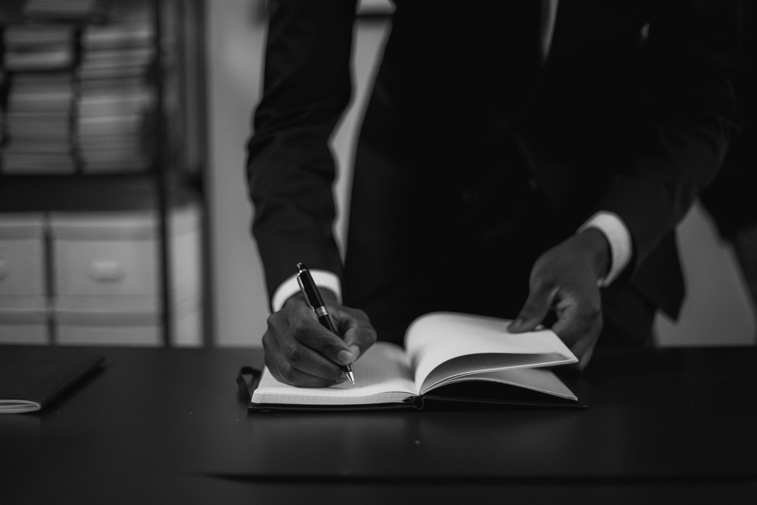 Close-up of a professional in a suit writing in an open notebook, symbolizing attention to regulatory detail and policy documentation.