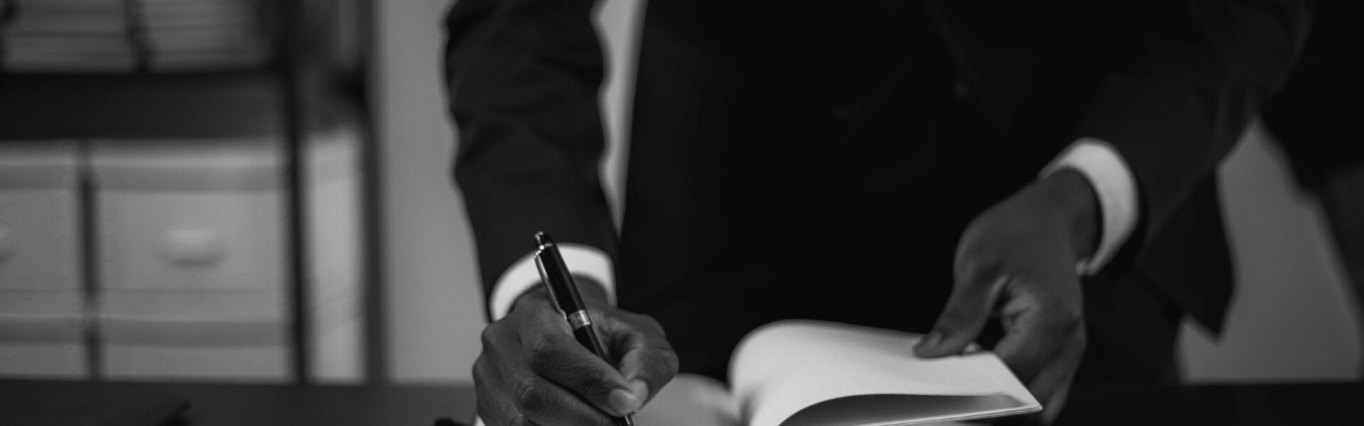 Close-up of a professional in a suit writing in an open notebook, symbolizing attention to regulatory detail and policy documentation.